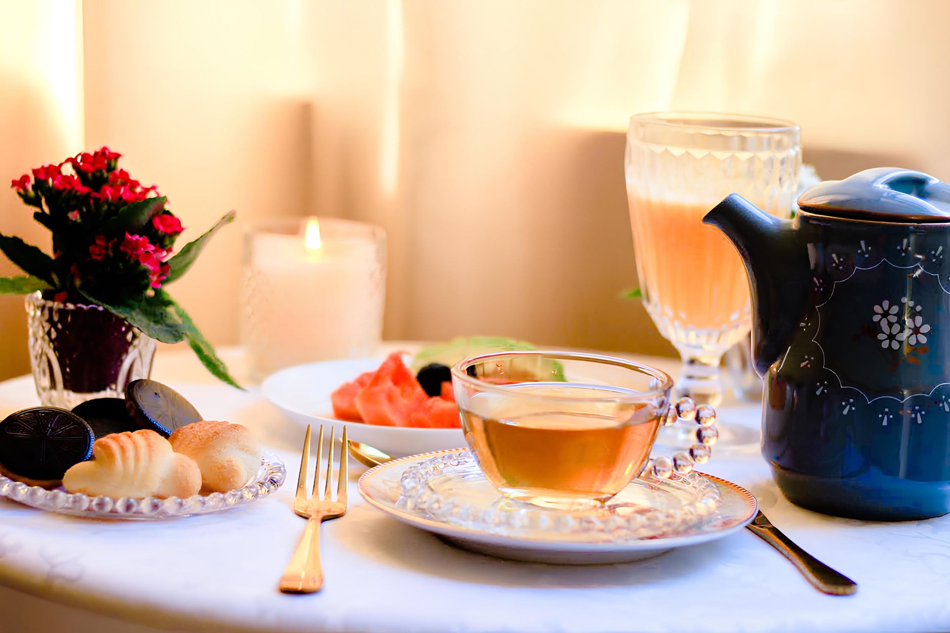 A warm and inviting tea setting with biscuits, candlelight, and fresh flowers.