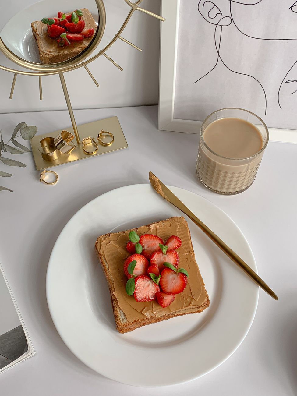 A stylish breakfast setup featuring peanut butter toast topped with fresh strawberries and a glass of milk.