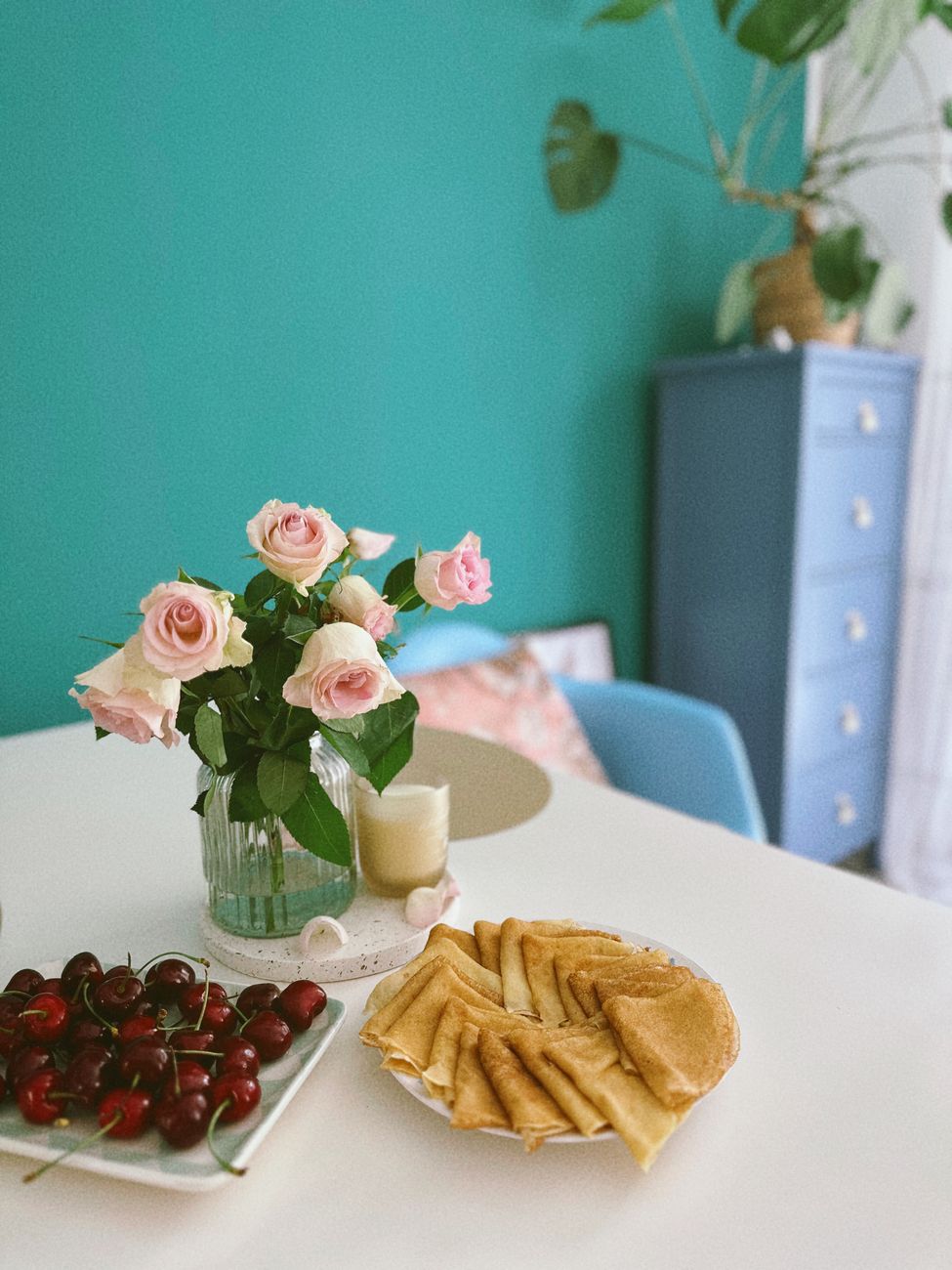 A cozy breakfast scene with pancakes, cherries, and pink roses on a white table.