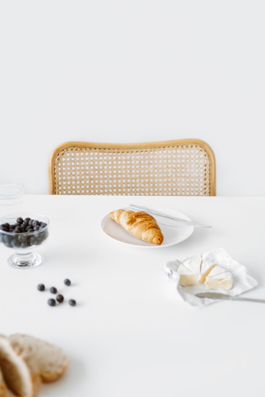 Minimalist breakfast setup featuring a croissant with blueberries and cheese on a white table.