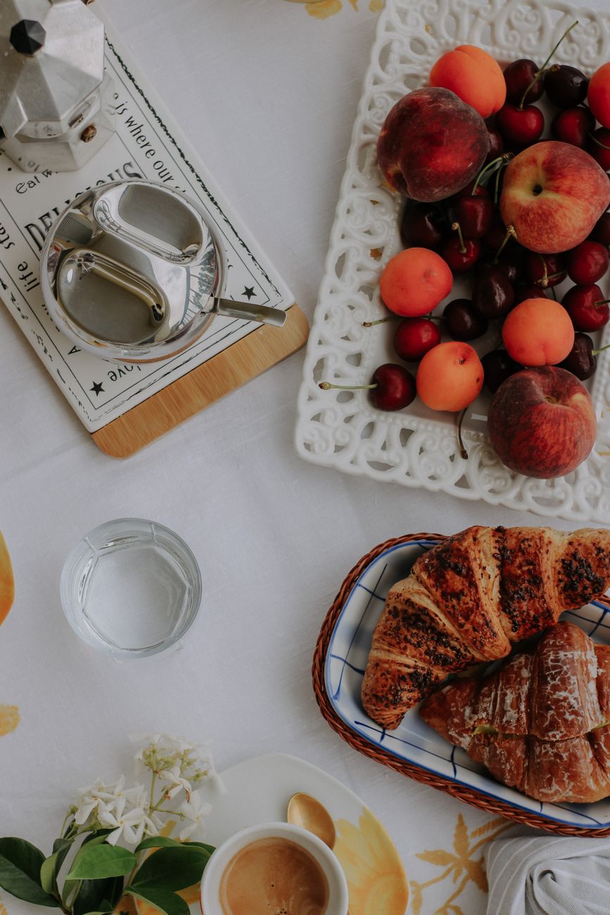 Elegant breakfast setting with croissants, fresh fruits, and coffee on a white table.