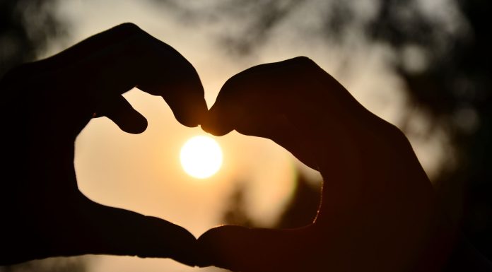 Yaz Ortası Aşk Rüzgarları: Kalbinizin Kapısını Kim Çalacak? Silhouette of hands forming a heart shape around a glowing sunset outdoors.